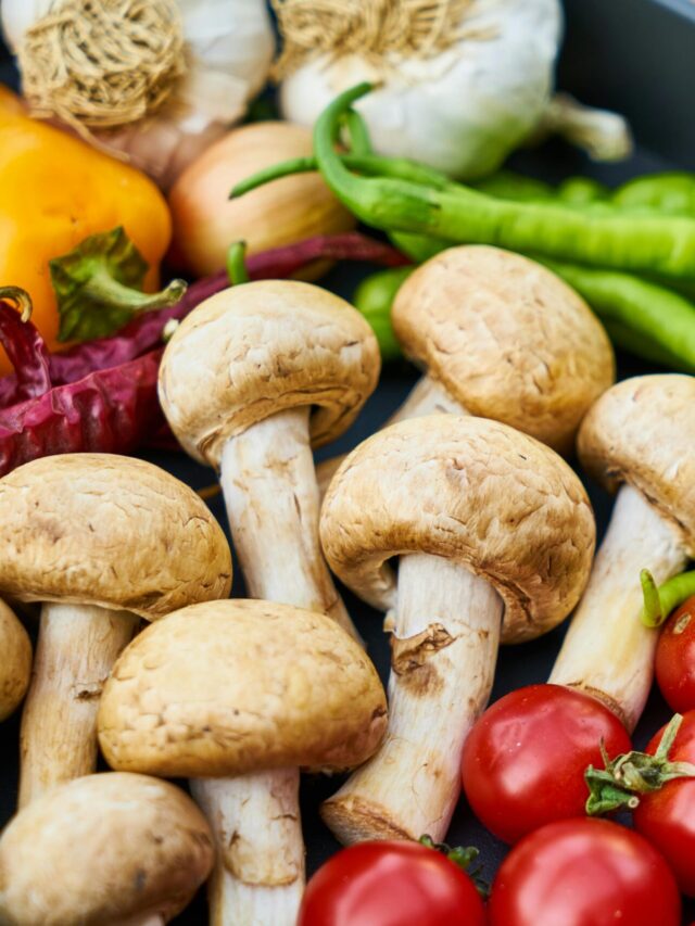 A close-up of various fresh vegetables and mushrooms in a pan on a wooden surface.