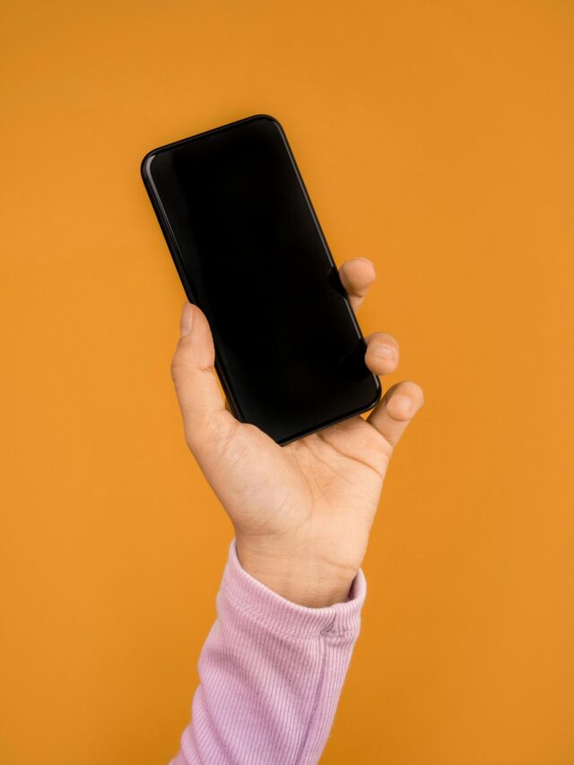 Close-up of a hand holding a smartphone against a bright orange backdrop, emphasizing modern technology.