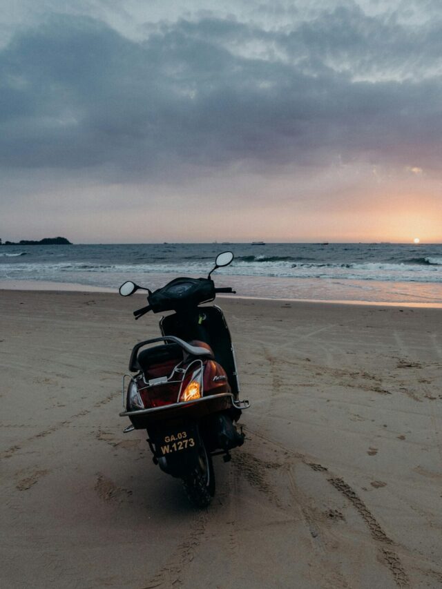 A motorcycle is parked on a tranquil Goa beach as the sun sets over the ocean. Perfect for travel inspiration.