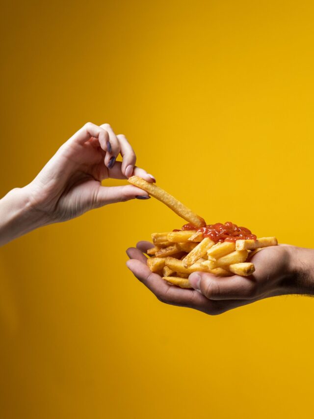 A close-up of hands sharing a delicious pile of french fries with ketchup against a yellow background.