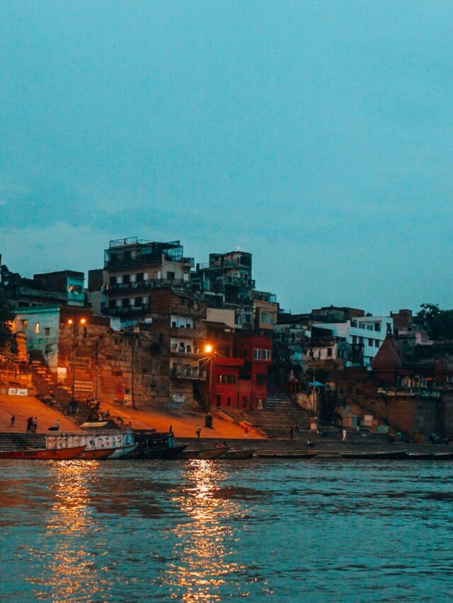 Scenic view of the illuminated Varanasi waterfront along the Ganges River at twilight.
