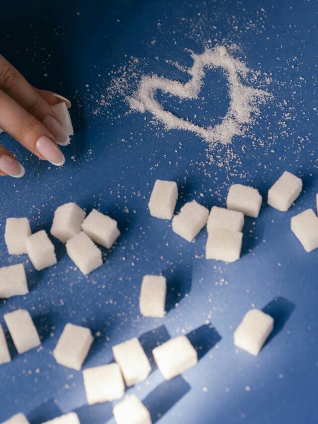 Top view of sugar cubes and a heart drawn in sugar on a blue surface with a hand nearby.