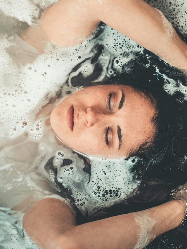 Calm and serene young woman enjoying a bubble bath with her eyes closed.