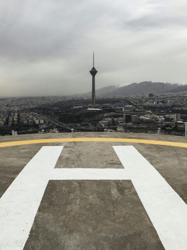 A dramatic view of Tehran's skyline featuring Milad Tower and a helipad under cloudy skies.